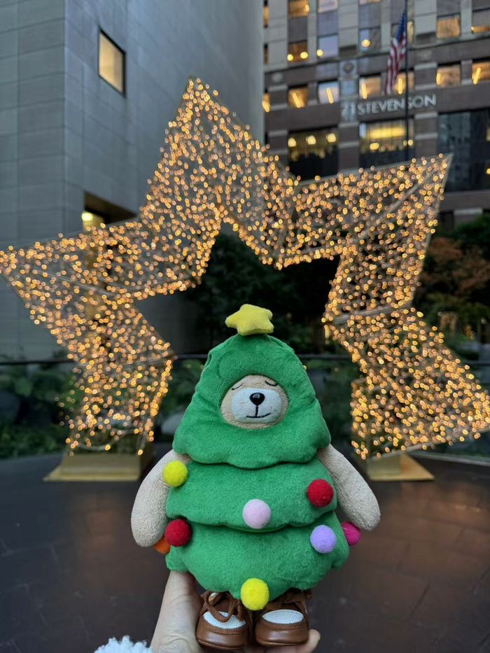 The real Fred Bear plush dressed as a Christmas tree in front of a lit star display